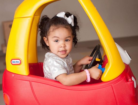 Sideway shot of little girl in red and yellow pedal kid car