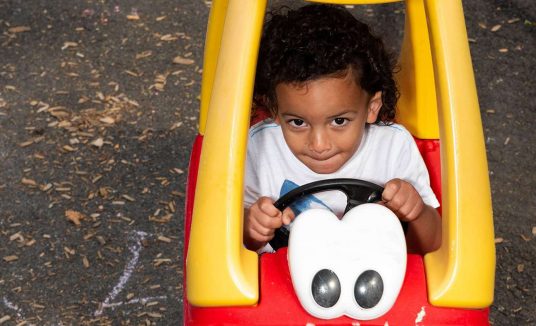 Little boy in small toy yellow and red car